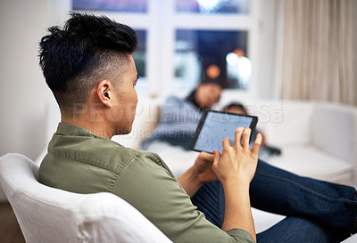 Buy stock photo Shot of a man using a digital tablet with his family in the background