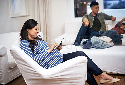 Buy stock photo Shot of a pregnant woman using a digital tablet with her family in the background