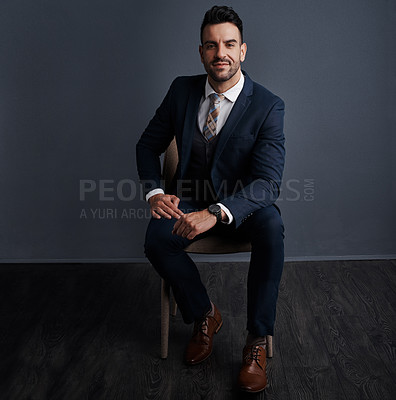 Buy stock photo Studio shot of a stylish young businessman sitting on a chair against a gray background