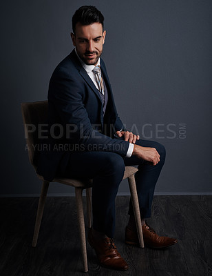 Buy stock photo Studio shot of a stylish young businessman sitting on a chair against a gray background