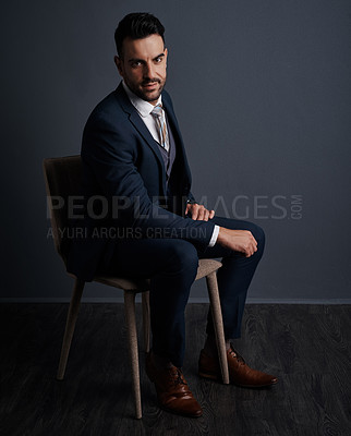 Buy stock photo Studio shot of a stylish young businessman sitting on a chair against a gray background