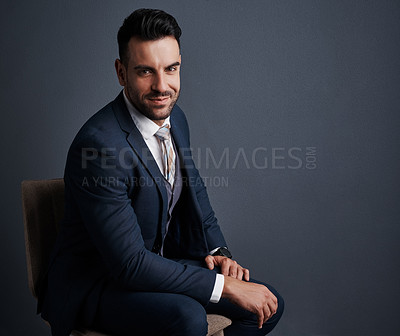 Buy stock photo Studio shot of a stylish young businessman sitting on a chair against a gray background