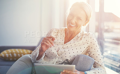 Buy stock photo Cropped shot of a mature woman using her digital tablet while relaxing at home