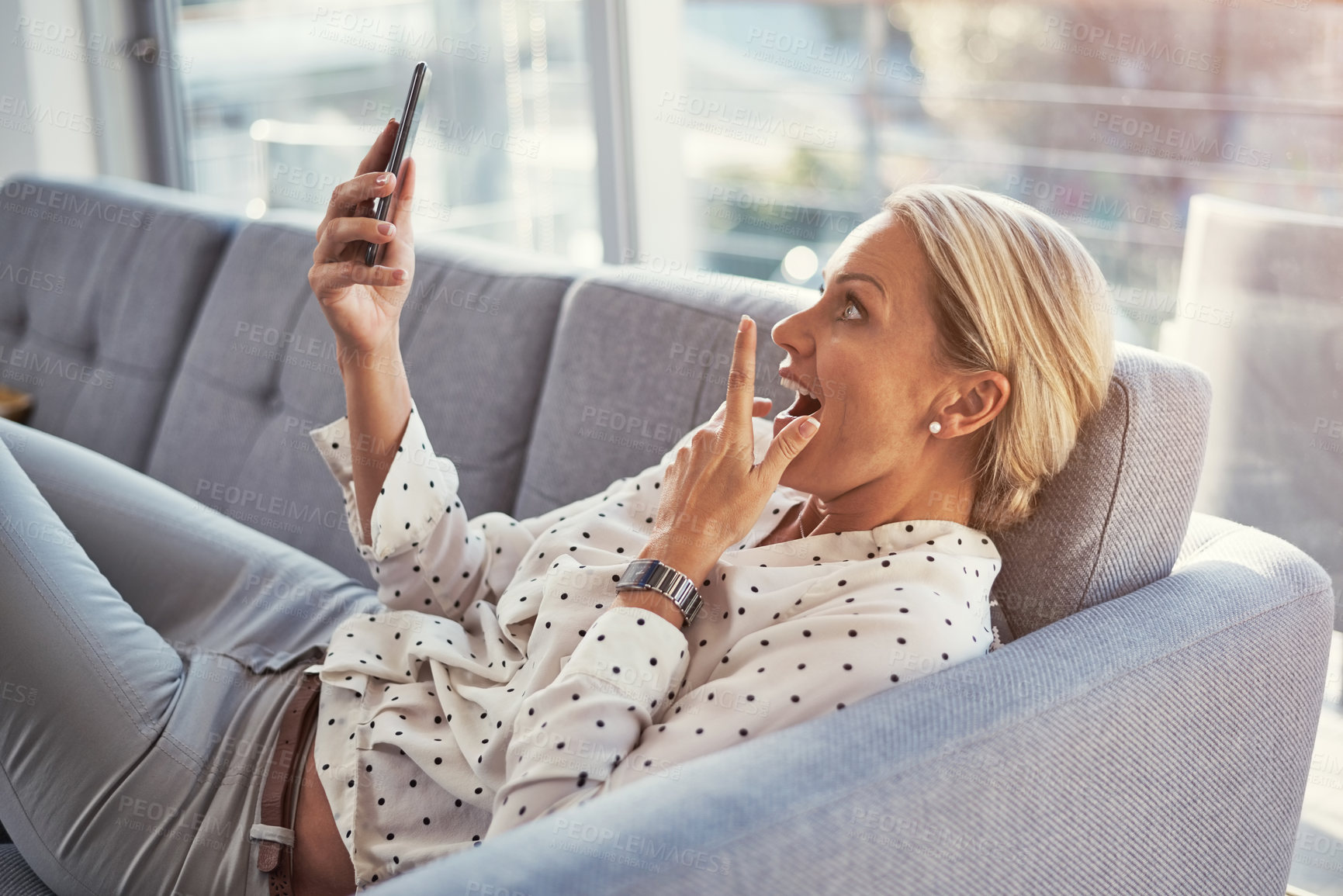 Buy stock photo Cropped shot of a mature woman using her cellphone while relaxing at home