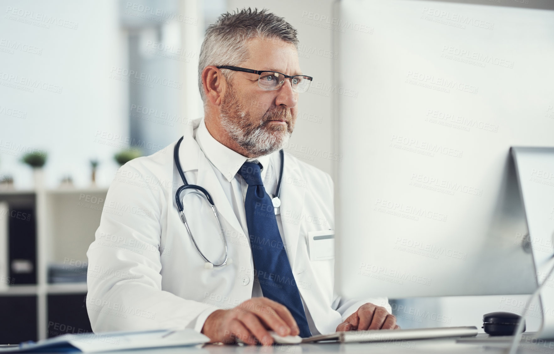 Buy stock photo Shot of a mature doctor using a computer at a desk in his office