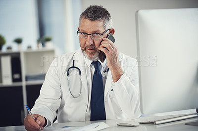 Buy stock photo Shot of a mature doctor using a mobile phone at a desk in his office