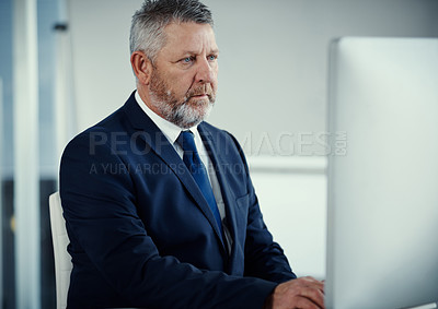 Buy stock photo Shot of a mature businessman using a computer at his desk in a modern office