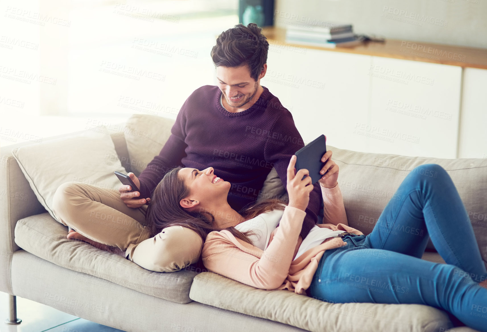 Buy stock photo Tablet, phone and couple relaxing on sofa for entertainment together in living room at home. Happy, love and people online networking on cellphone and digital technology in lounge at apartment.