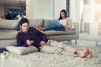 Buy stock photo Shot of a young couple relaxing in the living room while being on their mobile devices at home