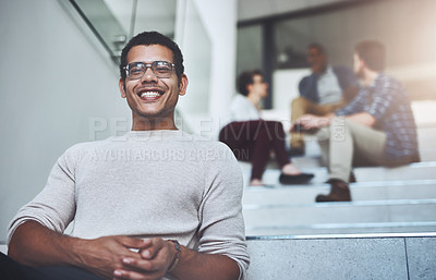 Buy stock photo Portrait of a young designer sitting on a staircase with his colleagues in the background