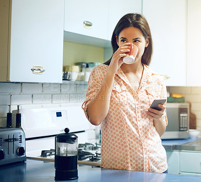 Buy stock photo Shot of an attractive young woman having coffee and using a mobile phone at home