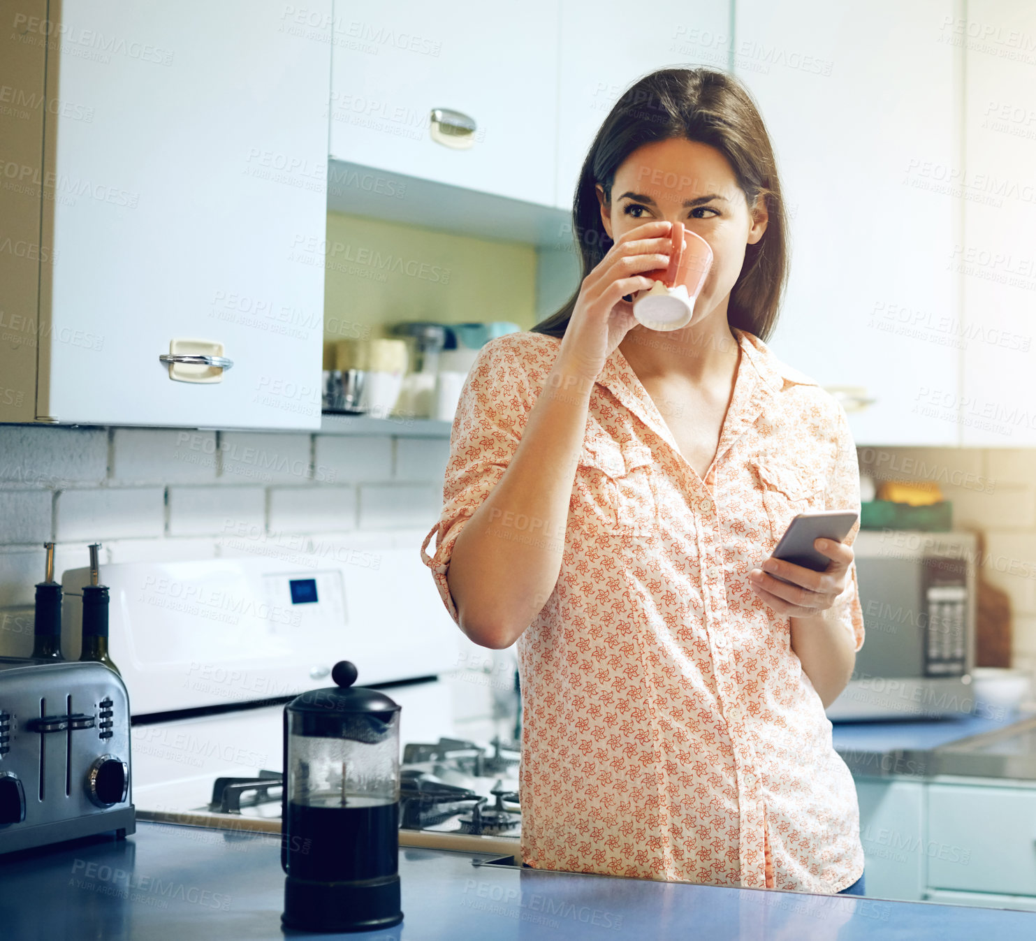 Buy stock photo Shot of an attractive young woman having coffee and using a mobile phone at home