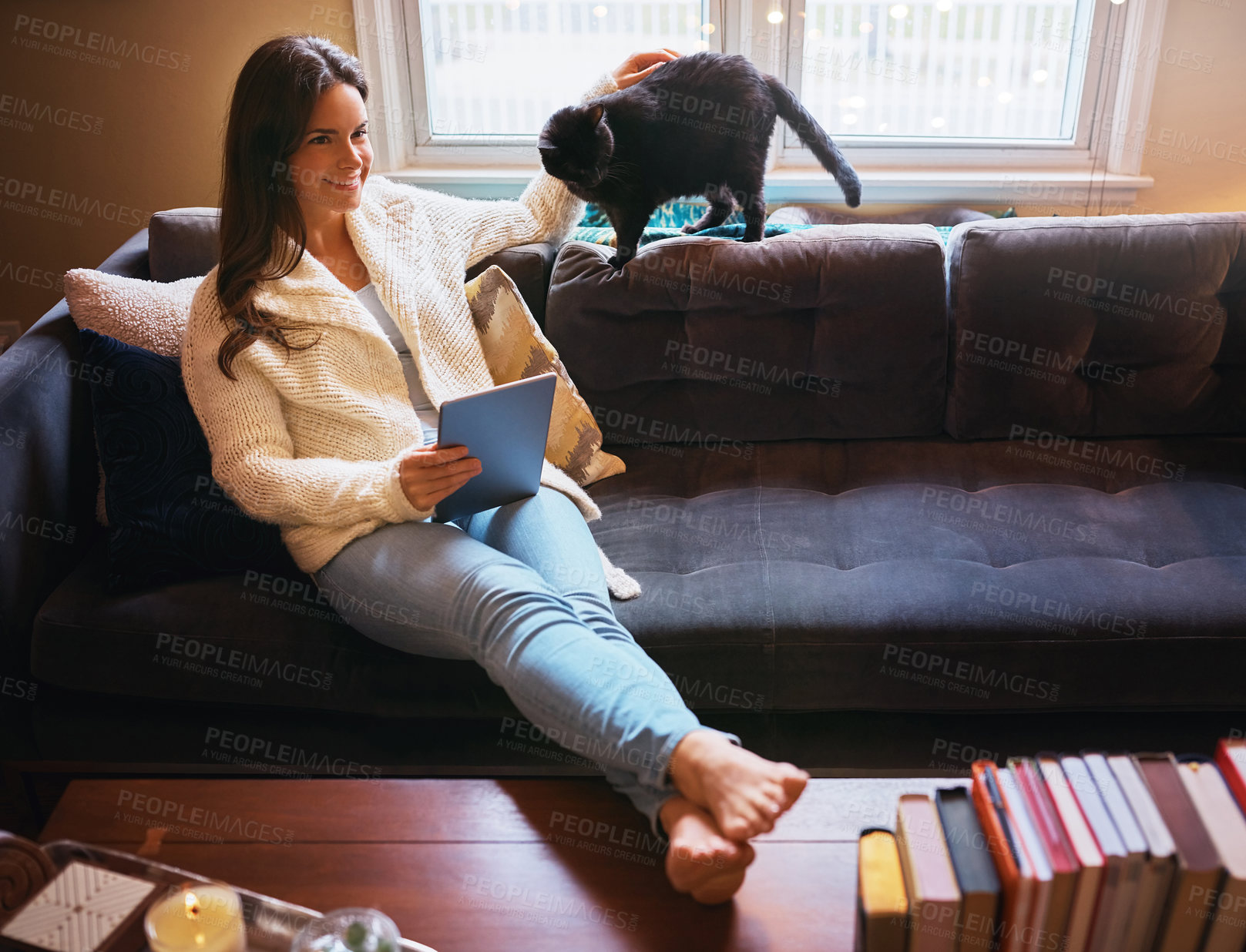 Buy stock photo Shot of an attractive young woman using a digital tablet on the sofa and affectionately stroking her cat