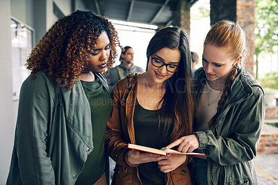 Buy stock photo Shot of a group of young students reading a notebook together on campus