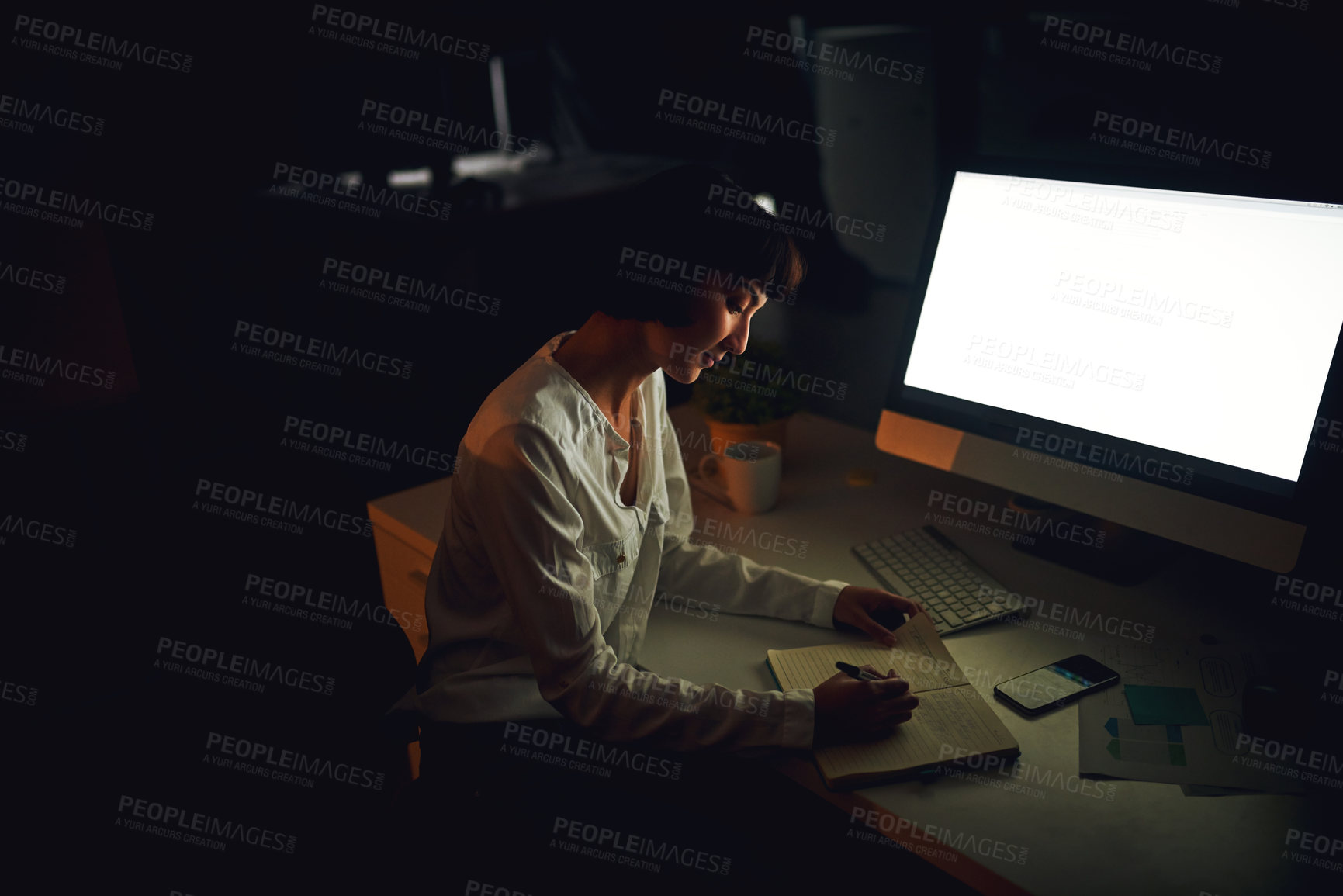 Buy stock photo Shot of a young businesswoman writing in a notebook during a late night at work