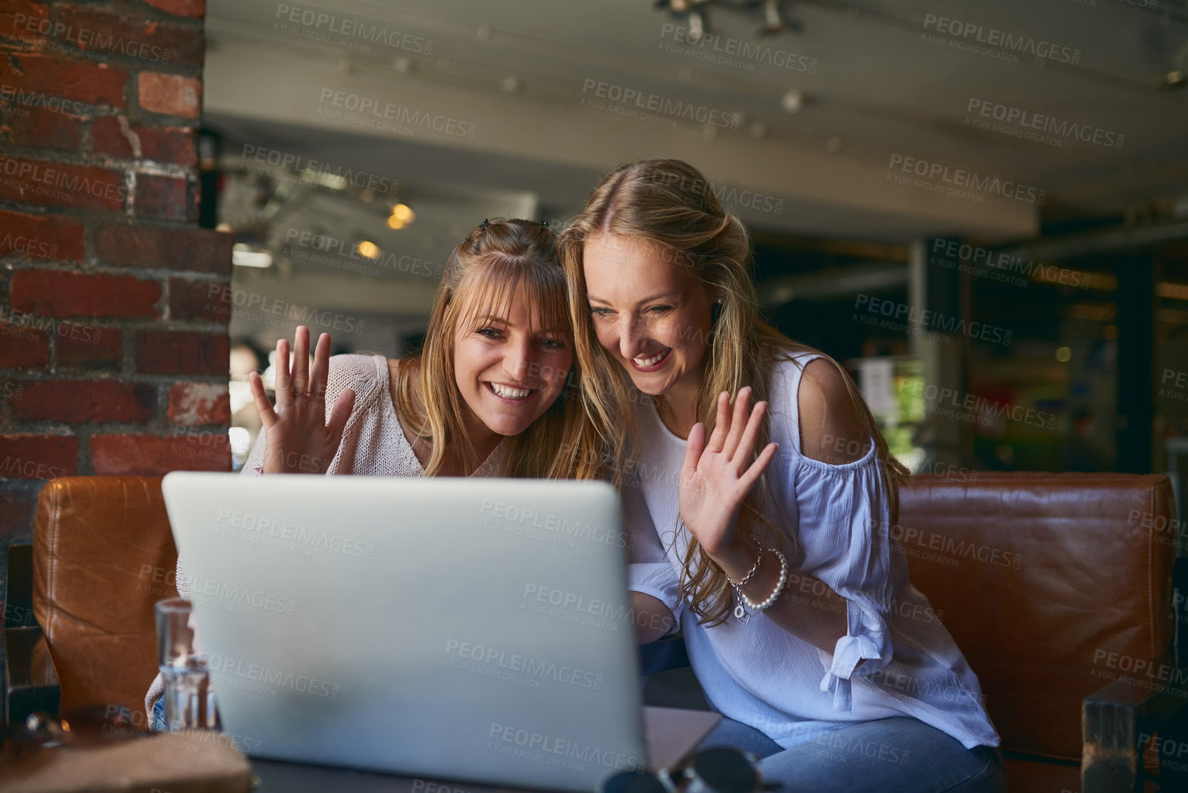 Buy stock photo Cropped shot of two attractive young girlfriends video chatting via laptop while sitting in a cafe