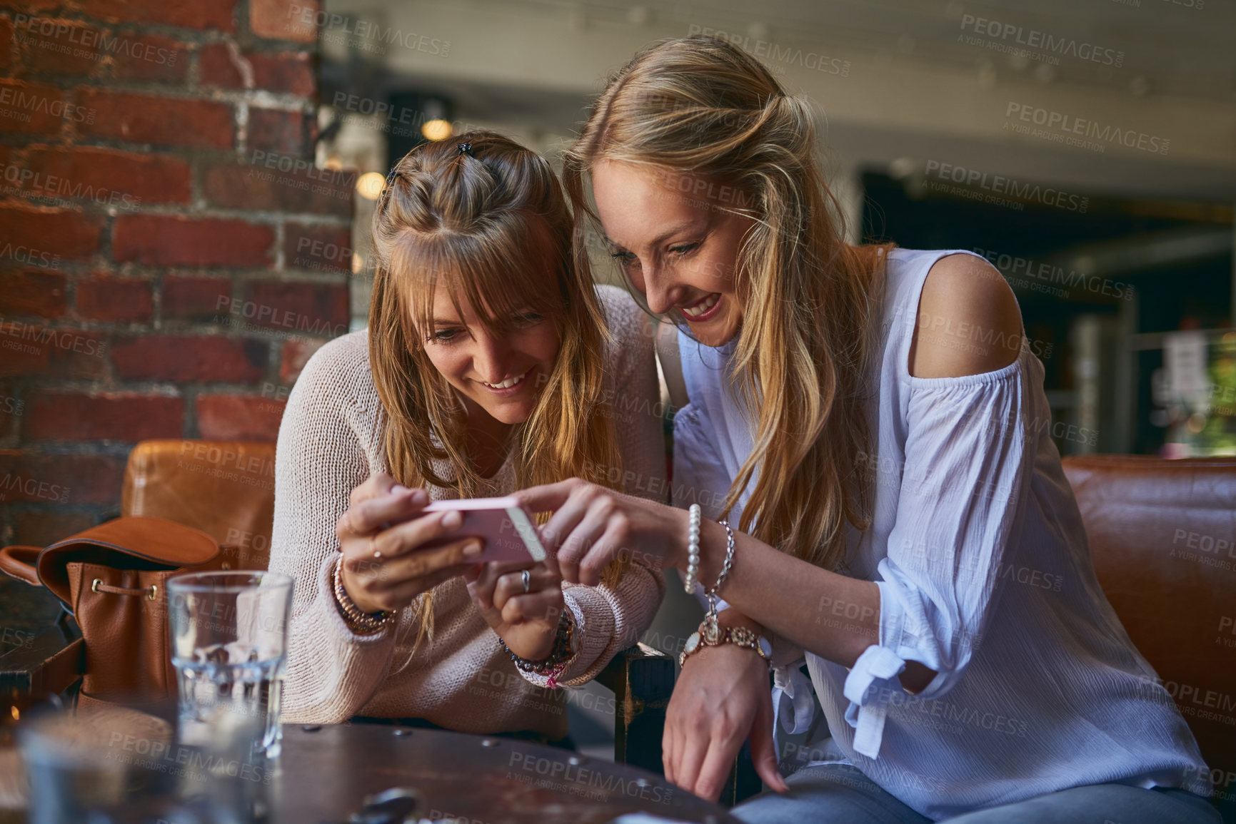 Buy stock photo Cropped shot of two attractive young girlfriends looking at a cellphone while sitting in a cafe