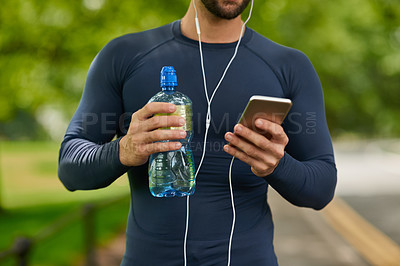 Buy stock photo Cropped shot of an unrecognizable male runner taking a drink of water and checking his messages during his workout