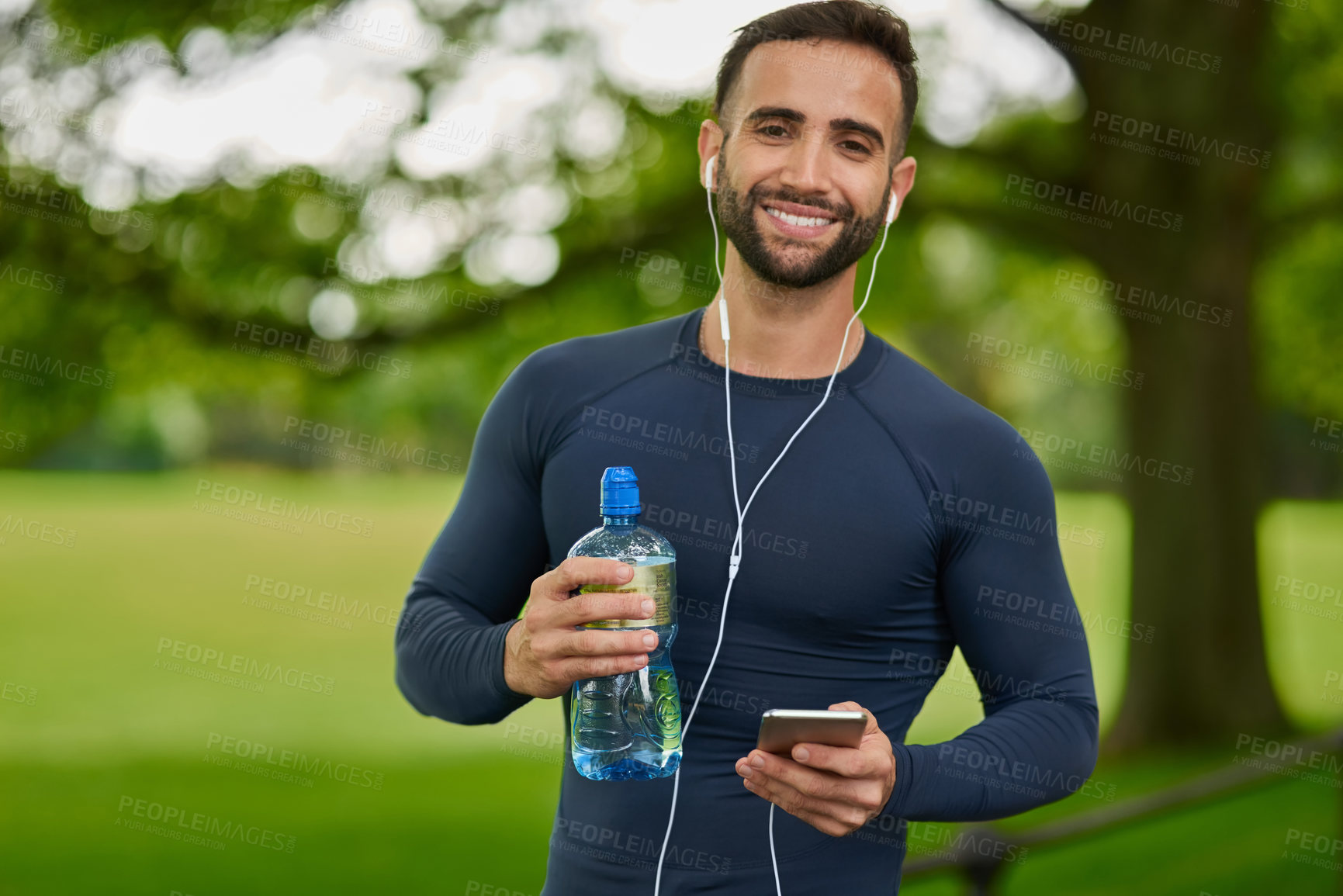 Buy stock photo Water, outdoor and portrait of man with earphones for listening to music, podcast or radio in nature. Happy, hydration and male athlete with audio tech for streaming running playlist on phone at park