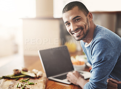 Buy stock photo Young man on a laptop while preparing a healthy meal at home. Portrait Happy smiling male browsing and learning on computer in the kitchen on how to cook. Guy alone checking online recipes on the web