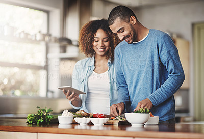 Buy stock photo Young, happy and romantic couple cooking healthy food together following recipes online on a tablet. Smiling husband and wife making dinner or lunch in the kitchen at home
