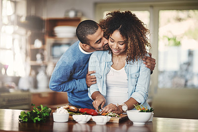 Buy stock photo Romantic, loving and caring boyfriend embraces his girlfriend and shows affection while they make food in the kitchen. A couple sharing a kiss and hug while cooking a meal or salad at home. 