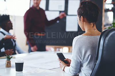 Buy stock photo Shot of a businesswoman texting on her cellphone during a meeting in an office