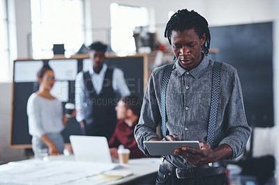 Buy stock photo Cropped shot of a handsome young businessman using a tablet in the office with his colleagues in the background