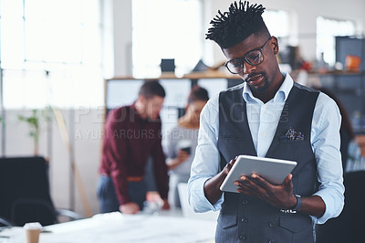 Buy stock photo Cropped shot of a handsome young businessman using a tablet in the office with his colleagues in the background