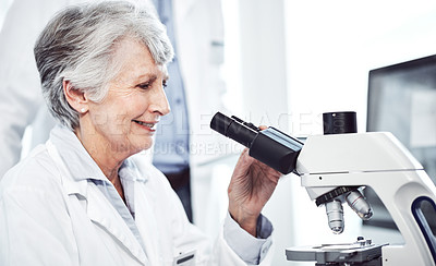 Buy stock photo Shot of a cheerful elderly female  scientist looking through a microscope while being seated in a laboratory