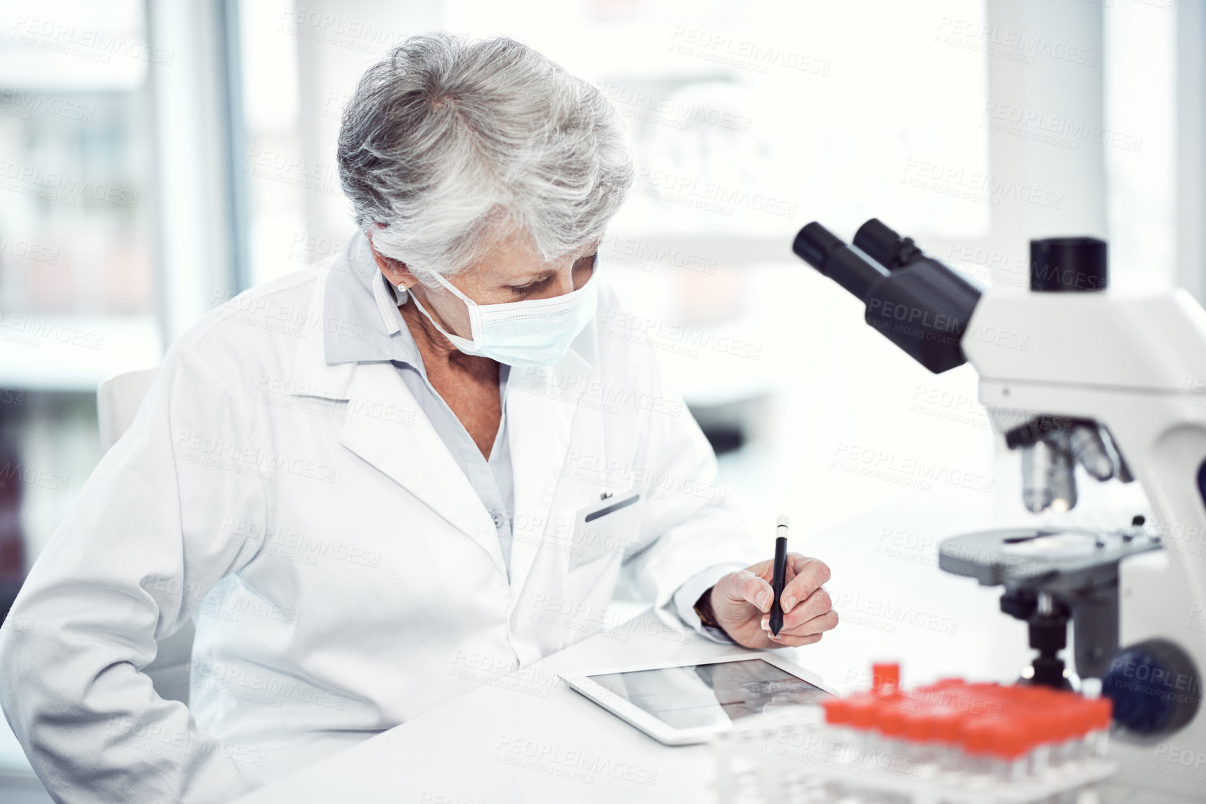 Buy stock photo Shot of a focused elderly female scientist working and making notes while wearing a doctor's mask inside of a laboratory