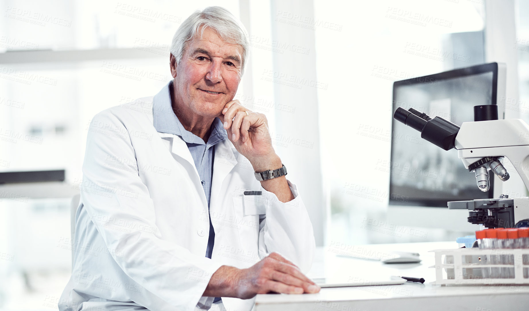 Buy stock photo Portrait of a cheerful elderly male scientist making notes while looking into the camera and being seated inside a laboratory