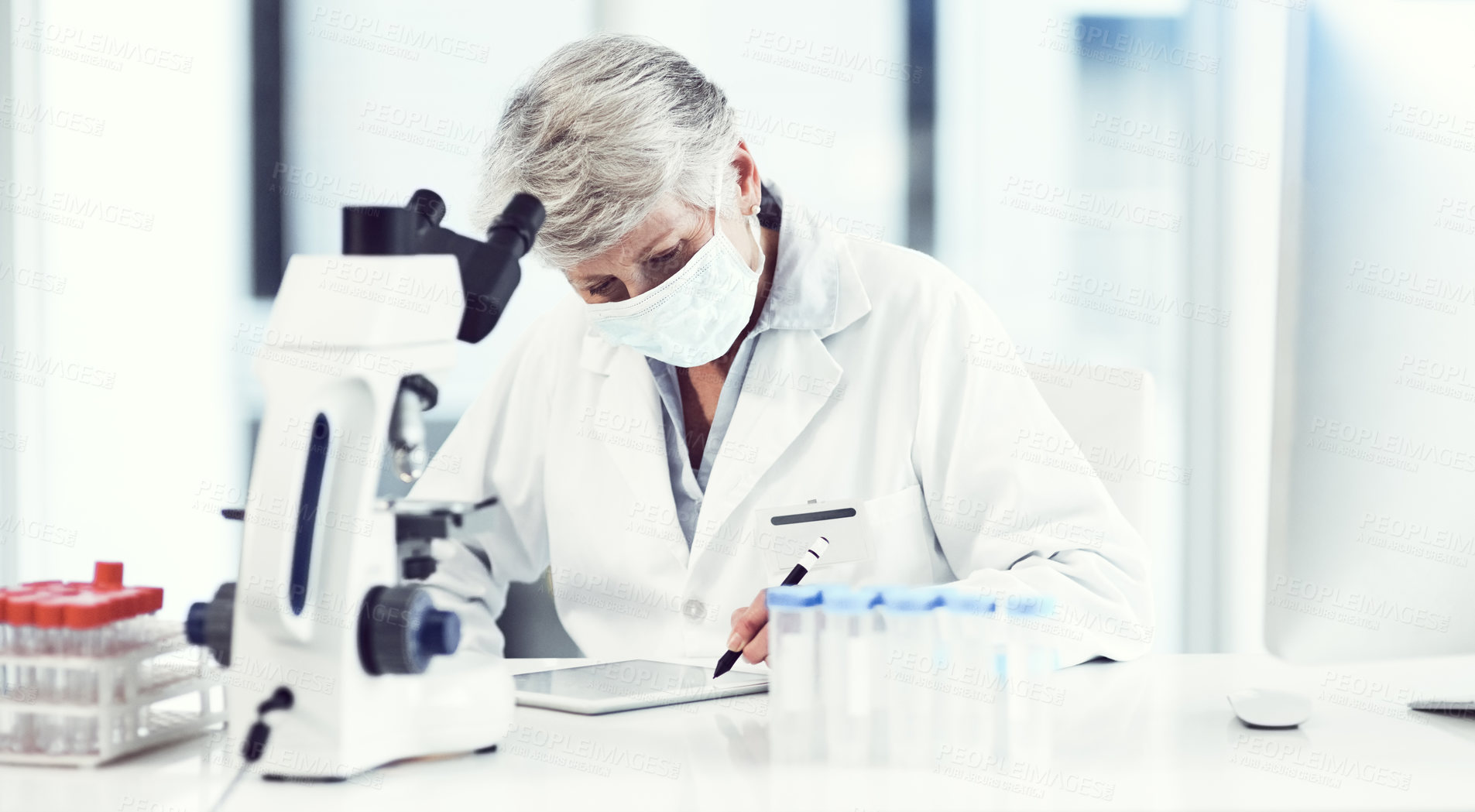 Buy stock photo Shot of a focused elderly female scientist working and making notes while wearing a doctor's mask inside of a laboratory
