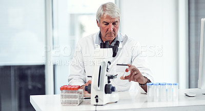 Buy stock photo Shot of a focused elderly male scientist holding up a test tube and making notes while being seated inside of a laboratory