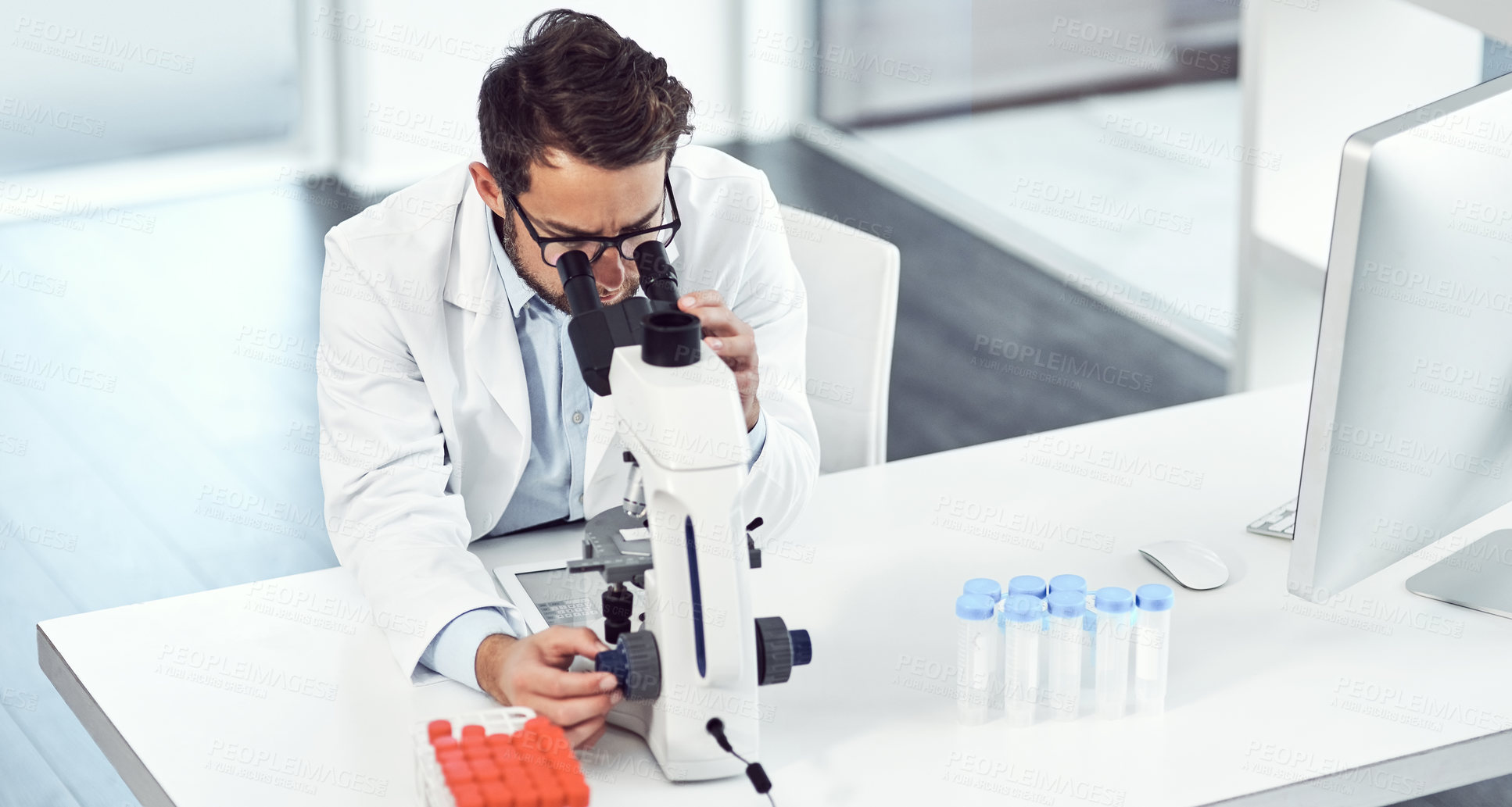 Buy stock photo Shot of a focused young male scientist looking through a microscope inside of a laboratory