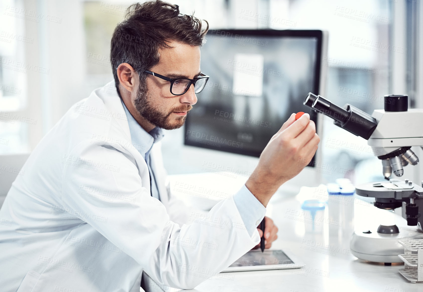 Buy stock photo Shot of a focused young male scientist examining a test tube while being seated inside a laboratory