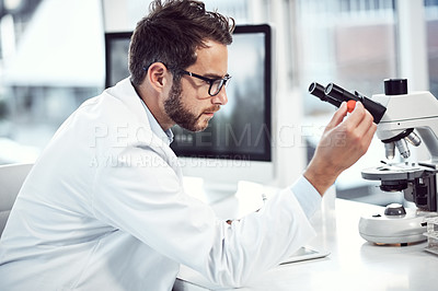 Buy stock photo Shot of a focused young male scientist examining a test tube while being seated inside a laboratory