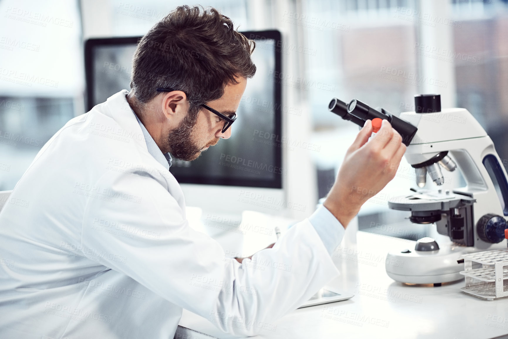 Buy stock photo Shot of a focused young male scientist making notes while holding up a test tube inside of a laboratory