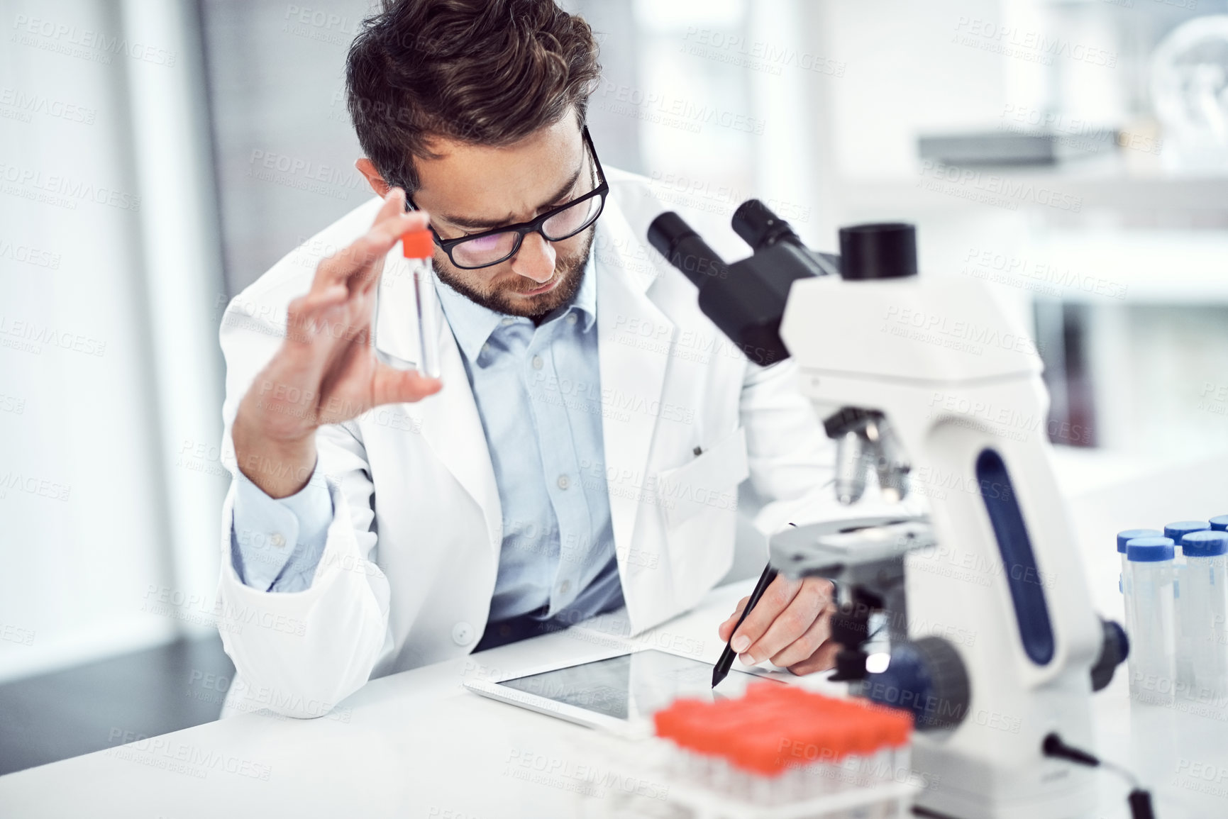 Buy stock photo Shot of a focused young male scientist making notes while holding up a test tube inside of a laboratory