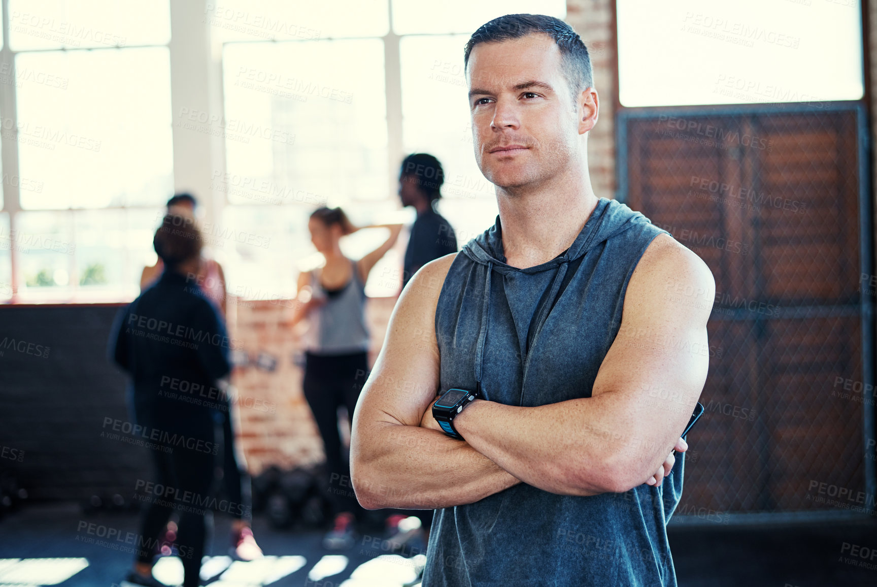 Buy stock photo Shot of a focused young man standing with arms folded while contemplating before a workout in a gym
