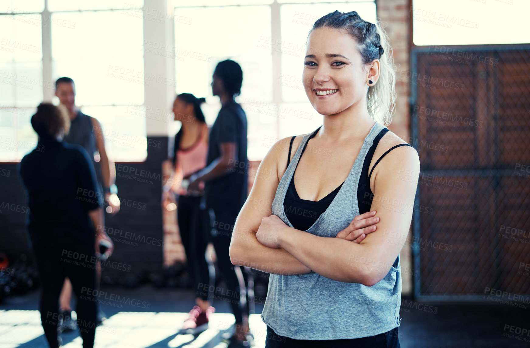 Buy stock photo Portrait of a cheerful young woman standing with her arms folded while looking into the camera before a workout in a gym
