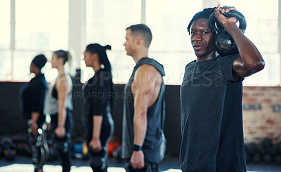 Buy stock photo Shot of a focused group of young people standing in a row and training with weights  while one looks into the camera in a gym