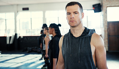 Buy stock photo Shot of a focused group of young people standing in a row and training with weights while one looks into the camera in a gym