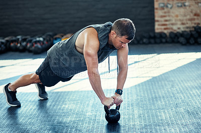 Buy stock photo Shot of a young man doing push ups with kettlebells in a gym