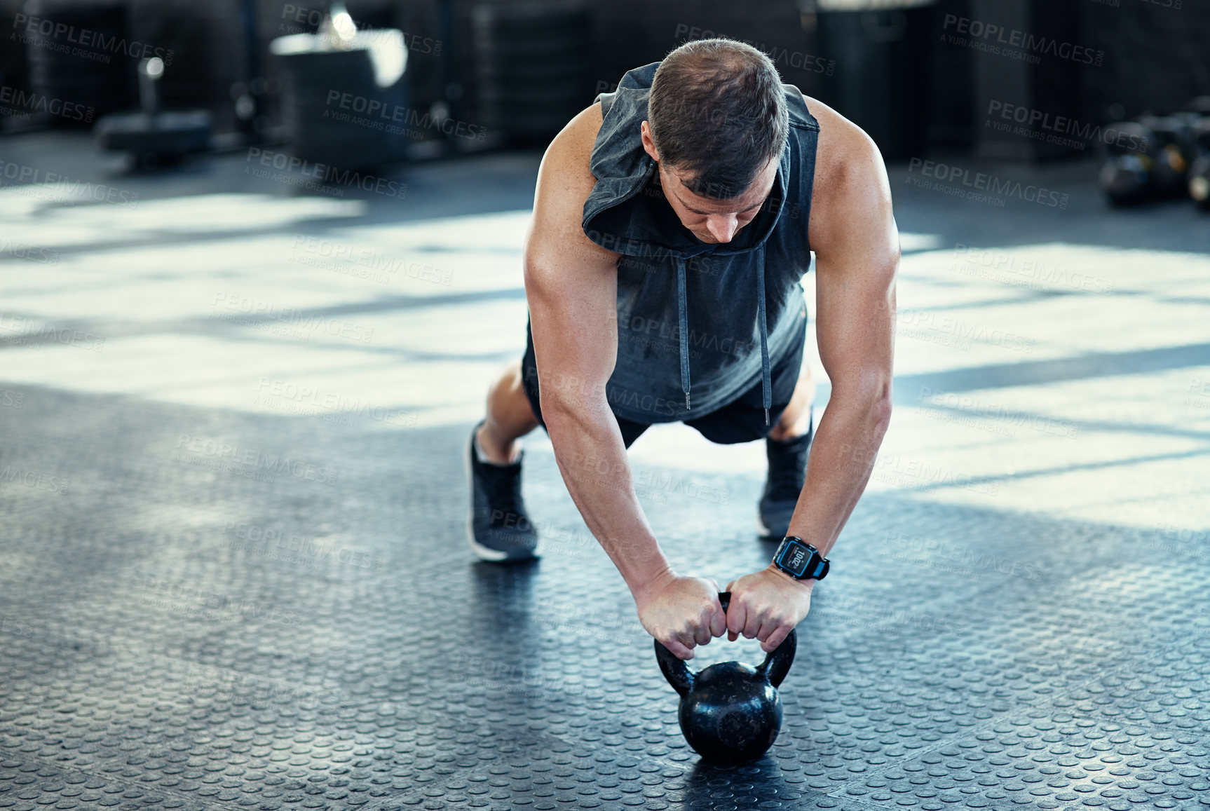 Buy stock photo Shot of a young man doing push ups with kettlebells in a gym