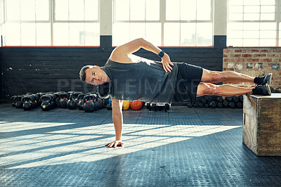 Buy stock photo Shot of a young man doing a side plank with a wooden block in a gym