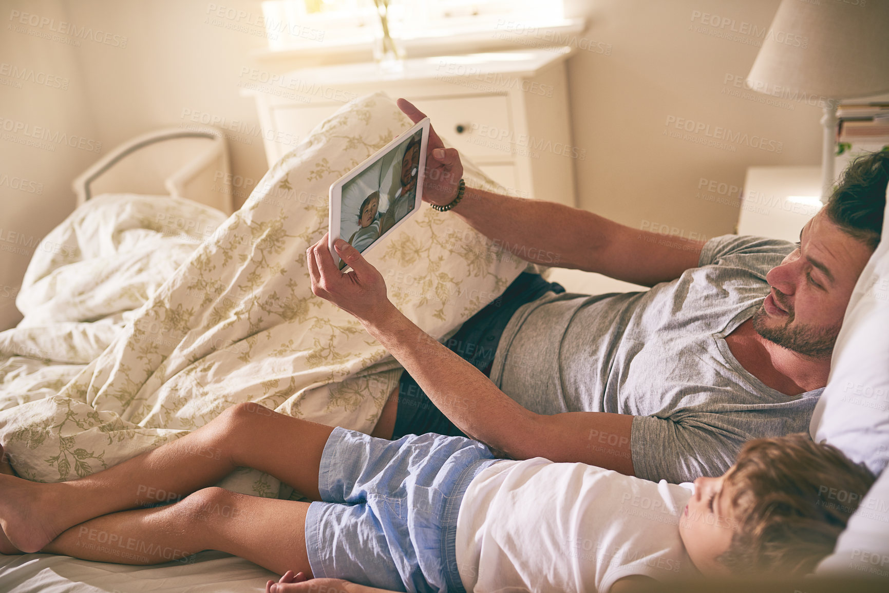 Buy stock photo Shot of a father and his little son using a digital tablet while lying in bed at home