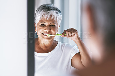 Buy stock photo Portrait of a cheerful mature woman brushing her teeth while looking into a mirror at home