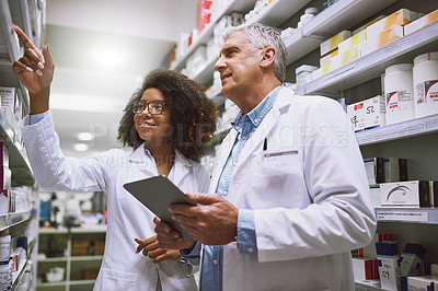 Buy stock photo Shot of two focused pharmacist walking around and doing stock inside of a pharmacy