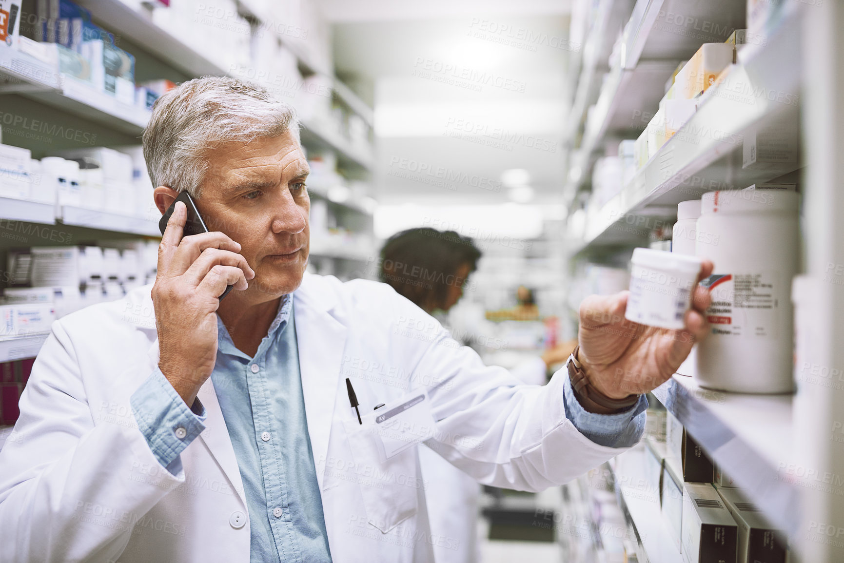 Buy stock photo Shot of a focused mature male pharmacist talking on his cellphone while reading the back of a medication box